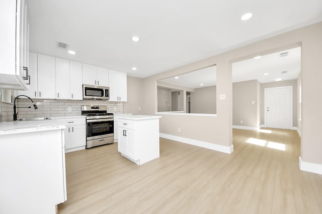 kitchen with light wood-style flooring, stainless steel appliances, a sink, decorative backsplash, and a center island