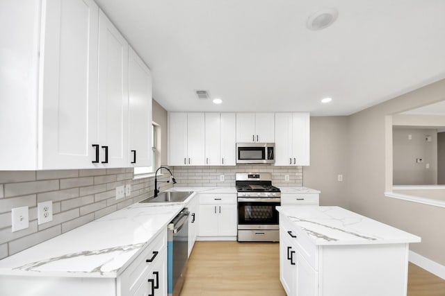 kitchen with light stone counters, stainless steel appliances, visible vents, light wood-style flooring, and a sink