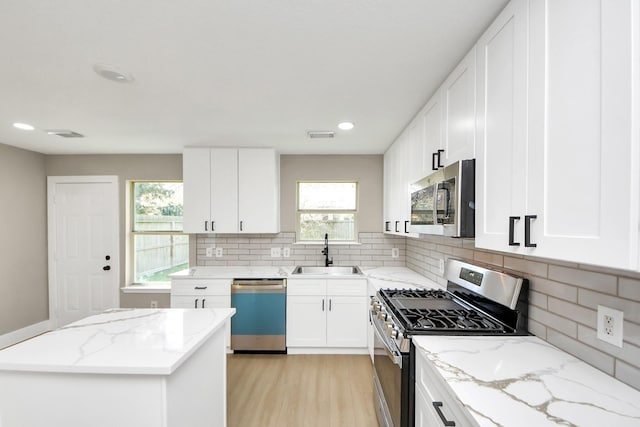 kitchen featuring stainless steel appliances, light wood-type flooring, a sink, and light stone counters