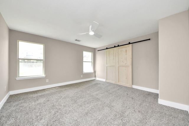 unfurnished bedroom featuring carpet floors, a barn door, visible vents, and baseboards