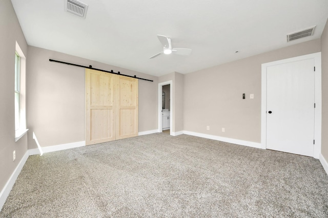 unfurnished bedroom with carpet, visible vents, baseboards, and a barn door