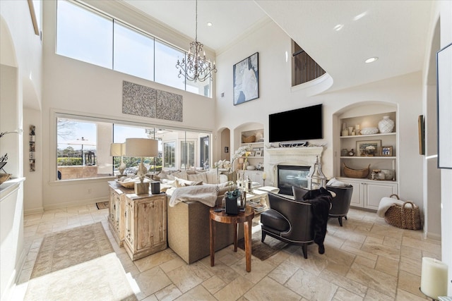 living area featuring built in shelves, baseboards, a premium fireplace, an inviting chandelier, and stone tile flooring