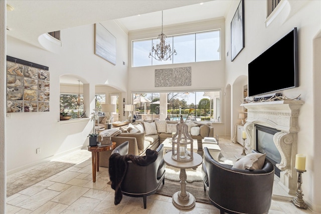 living area with baseboards, an inviting chandelier, ornamental molding, stone tile flooring, and a glass covered fireplace