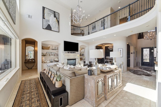 living room with visible vents, built in shelves, a notable chandelier, and a glass covered fireplace