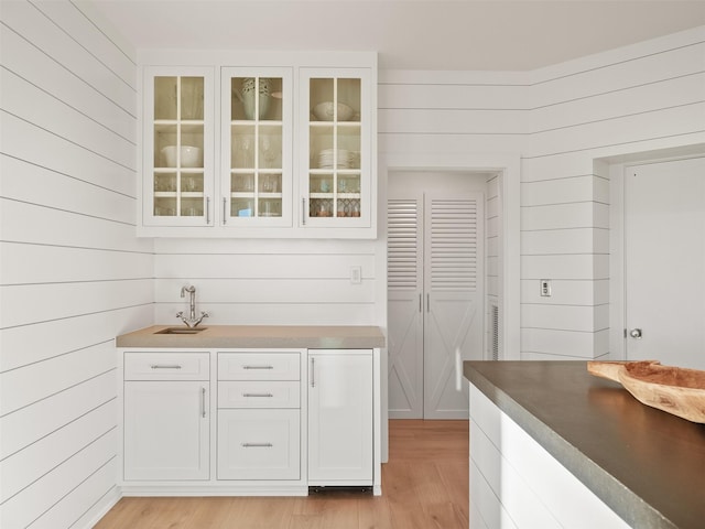 bar featuring light wood finished floors, a sink, and wooden walls