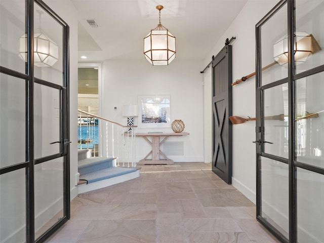 hallway featuring stairs, a barn door, visible vents, and baseboards