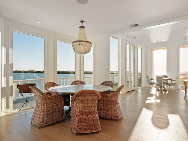 dining area featuring french doors, a water view, visible vents, wood finished floors, and a chandelier