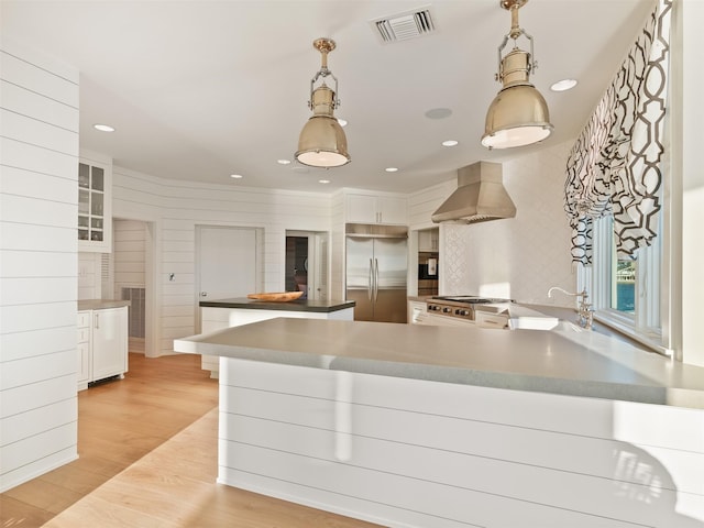 kitchen with visible vents, white cabinets, light wood-style flooring, wall chimney range hood, and built in fridge