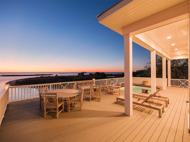 deck at dusk featuring a water view and outdoor dining space