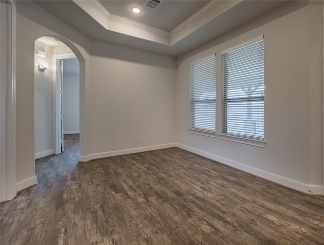 spare room with crown molding, baseboards, dark wood finished floors, a tray ceiling, and arched walkways