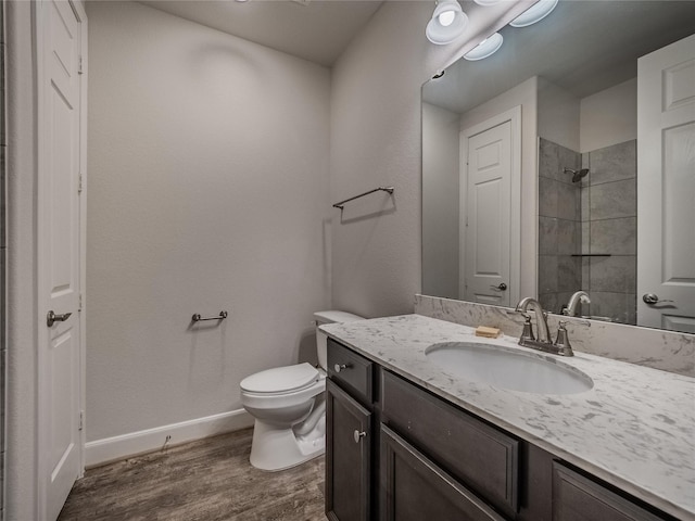 bathroom featuring toilet, wood finished floors, tiled shower, baseboards, and vanity