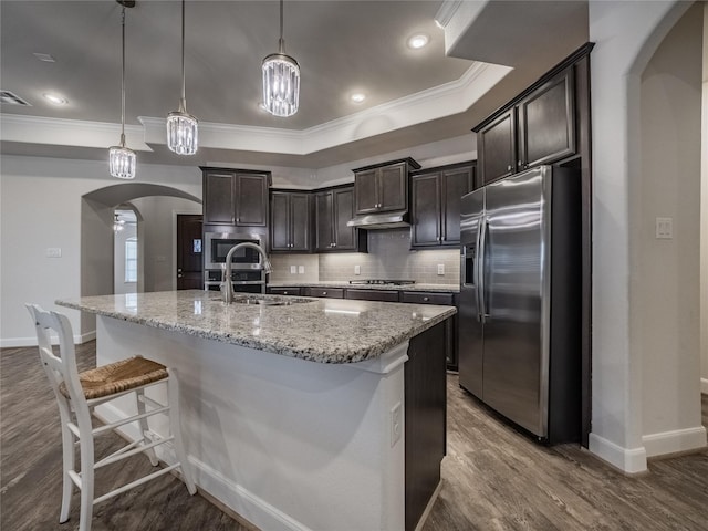 kitchen featuring under cabinet range hood, tasteful backsplash, arched walkways, appliances with stainless steel finishes, and dark brown cabinets