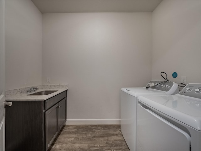 laundry room with wood finished floors, baseboards, cabinet space, a sink, and washing machine and dryer