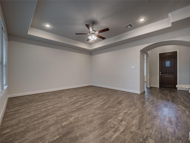 spare room with a tray ceiling, dark wood-style floors, visible vents, and arched walkways