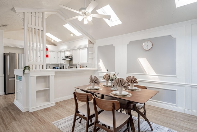 dining space with ceiling fan, vaulted ceiling with skylight, a decorative wall, visible vents, and light wood-type flooring