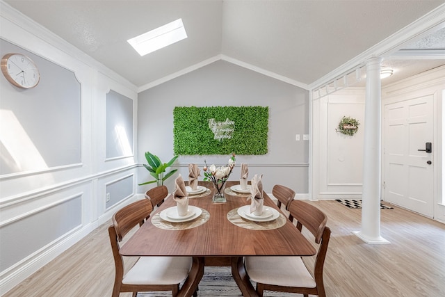 dining room with vaulted ceiling with skylight, a decorative wall, decorative columns, and light wood-style floors