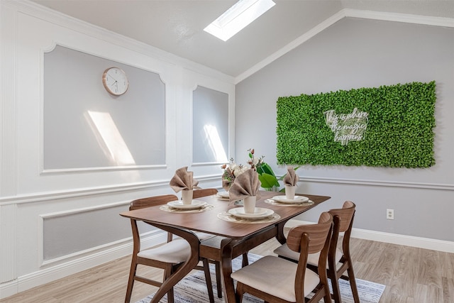 dining room featuring vaulted ceiling with skylight, light wood finished floors, and baseboards