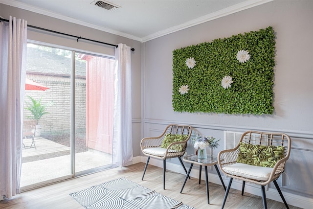 living area with a decorative wall, a wainscoted wall, visible vents, ornamental molding, and light wood finished floors