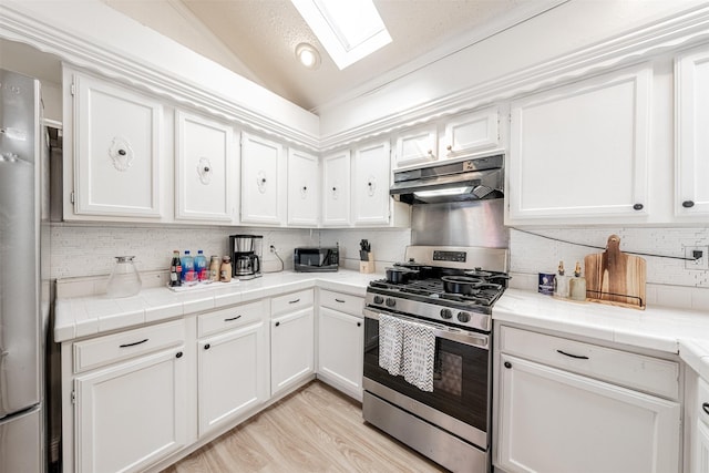 kitchen with lofted ceiling with skylight, gas stove, white cabinets, and under cabinet range hood