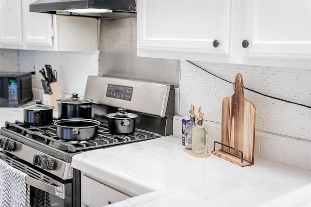 kitchen with stainless steel gas stove, white cabinets, decorative backsplash, tile countertops, and range hood