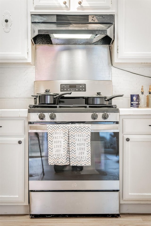 kitchen featuring white cabinets, ventilation hood, light countertops, and gas stove