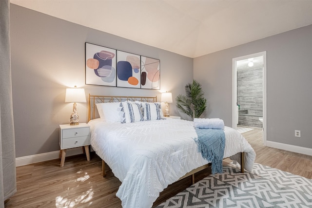 bedroom with ensuite bathroom, vaulted ceiling, baseboards, and wood finished floors