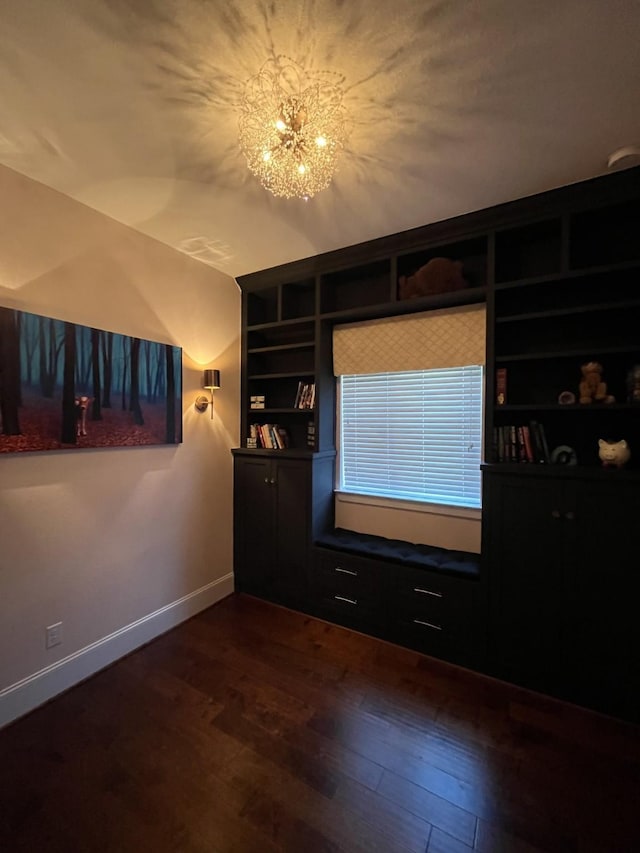 unfurnished room featuring dark wood-style floors, baseboards, built in features, and a notable chandelier