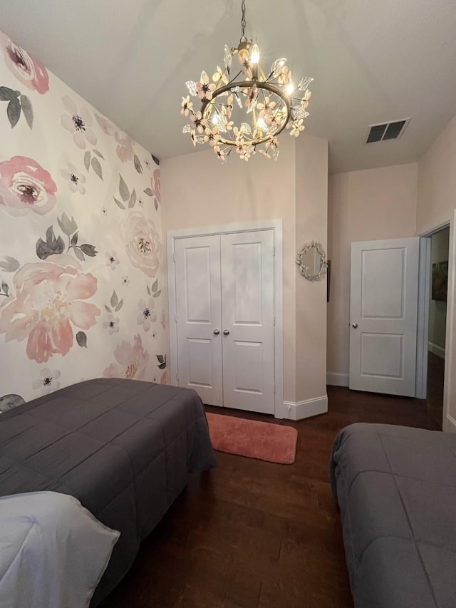 bedroom with a closet, visible vents, wood finished floors, a chandelier, and baseboards