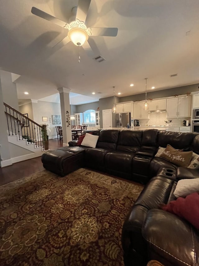 living room featuring ceiling fan, visible vents, baseboards, stairs, and decorative columns