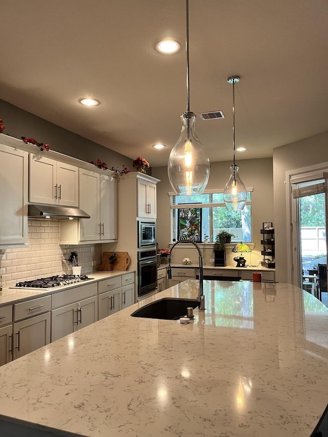 kitchen with under cabinet range hood, a sink, visible vents, appliances with stainless steel finishes, and backsplash