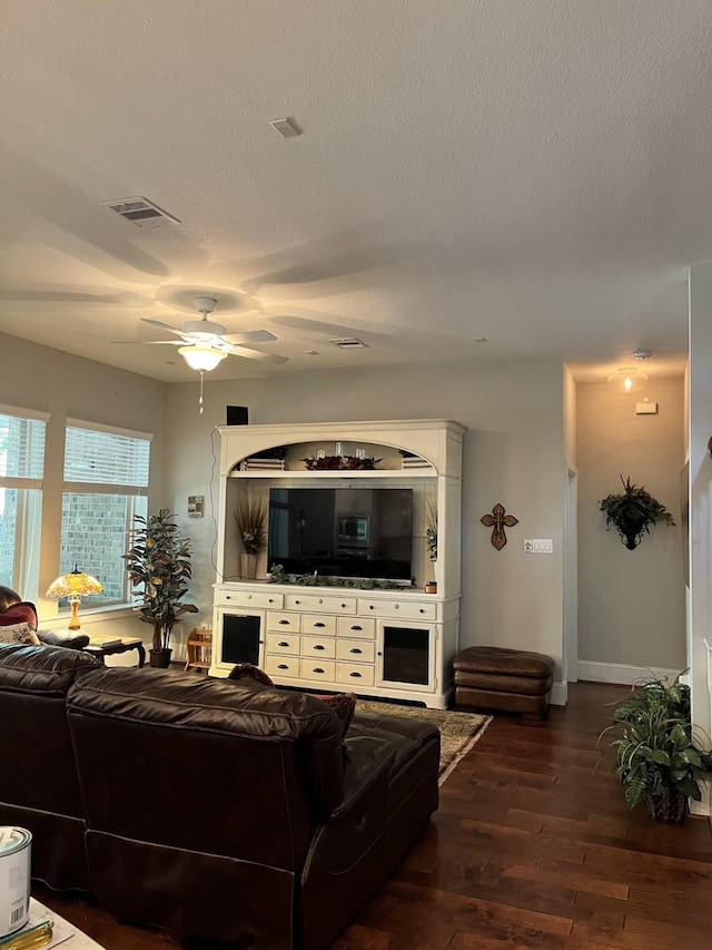 living room with ceiling fan, a textured ceiling, visible vents, baseboards, and dark wood-style floors