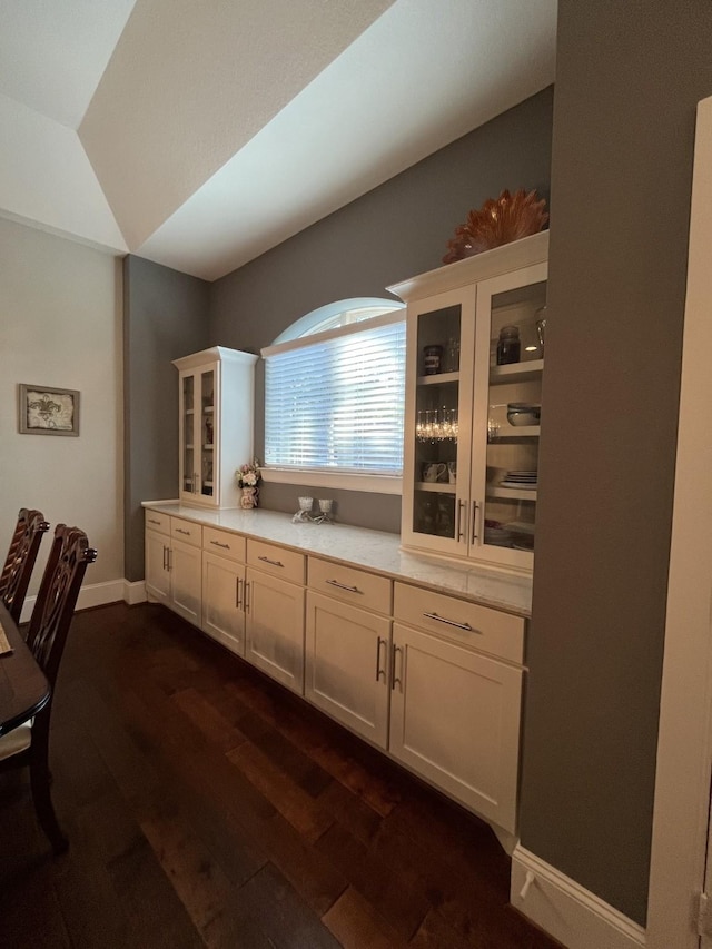 kitchen with dark wood-type flooring, light countertops, glass insert cabinets, and baseboards