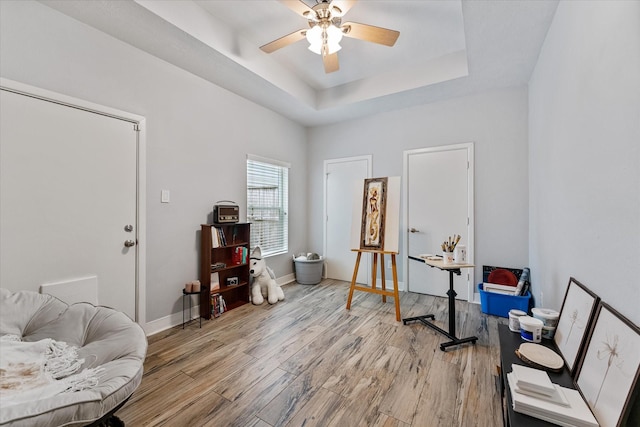 interior space featuring a tray ceiling, light wood-style flooring, baseboards, and ceiling fan