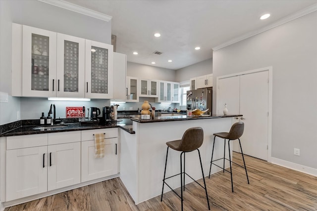 kitchen with light wood-type flooring, a sink, a peninsula, white cabinets, and stainless steel fridge with ice dispenser