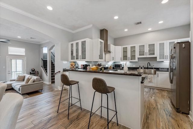 kitchen featuring visible vents, light wood finished floors, a peninsula, stainless steel appliances, and wall chimney range hood