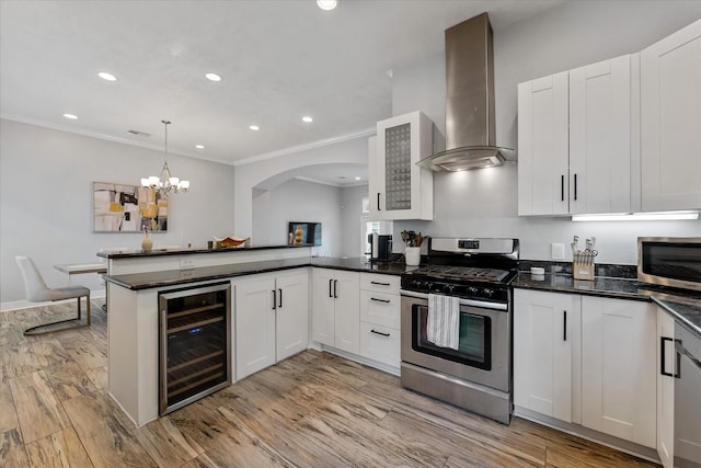 kitchen with beverage cooler, light wood-style floors, a peninsula, appliances with stainless steel finishes, and wall chimney range hood