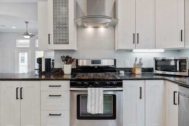 kitchen with ceiling fan, dark stone counters, white cabinets, stainless steel appliances, and wall chimney exhaust hood