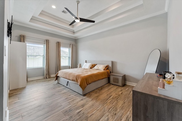 bedroom featuring light wood-type flooring, visible vents, ornamental molding, a tray ceiling, and baseboards