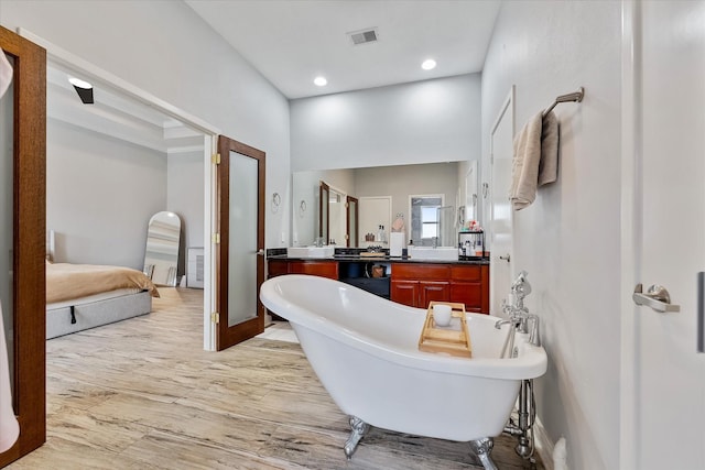 ensuite bathroom with vanity, wood finished floors, visible vents, a soaking tub, and recessed lighting