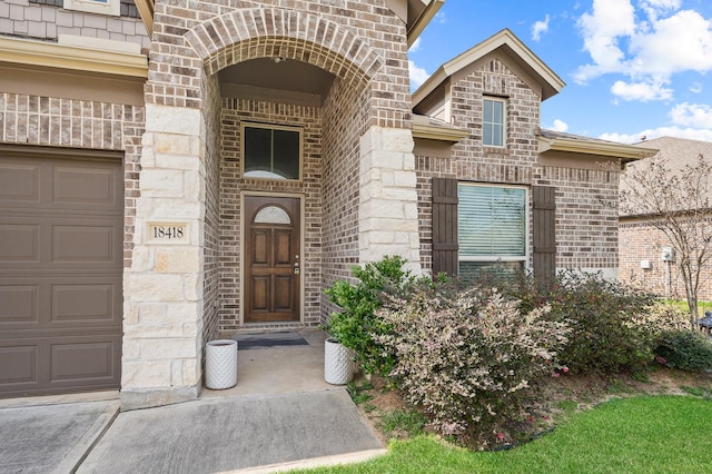 doorway to property with stone siding, brick siding, and an attached garage