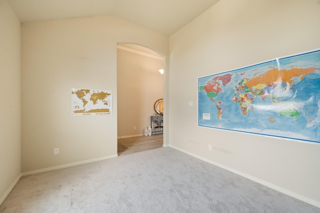 carpeted spare room with lofted ceiling, baseboards, and arched walkways