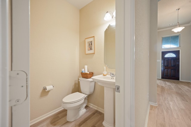 half bath featuring toilet, wood finish floors, a sink, baseboards, and crown molding