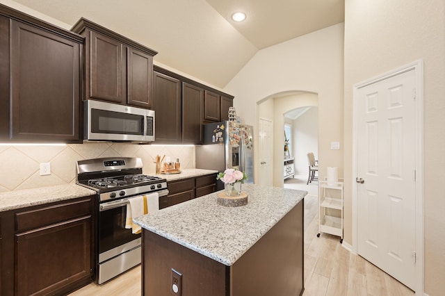 kitchen with dark brown cabinetry, arched walkways, lofted ceiling, appliances with stainless steel finishes, and backsplash