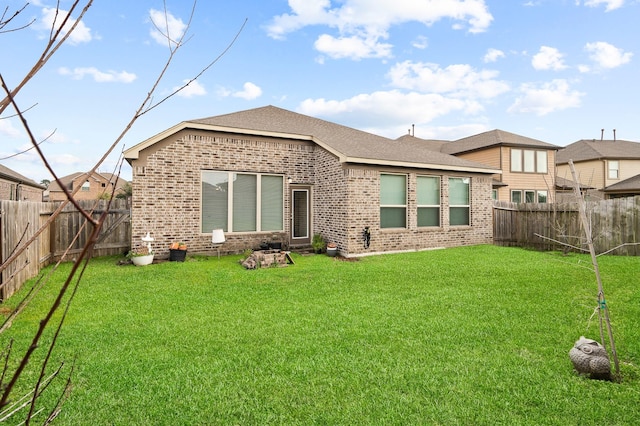 rear view of house featuring roof with shingles, brick siding, a lawn, and a fenced backyard