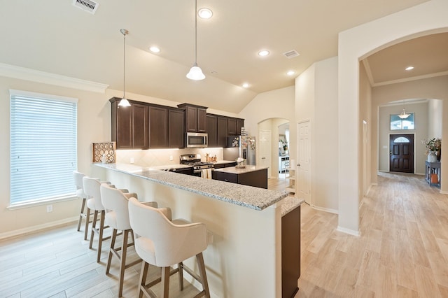 kitchen with arched walkways, dark brown cabinetry, visible vents, appliances with stainless steel finishes, and a kitchen bar