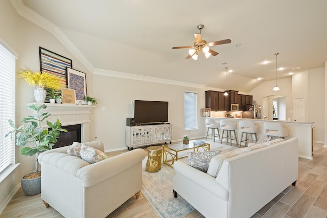 living room with vaulted ceiling, ceiling fan, light wood finished floors, and a glass covered fireplace