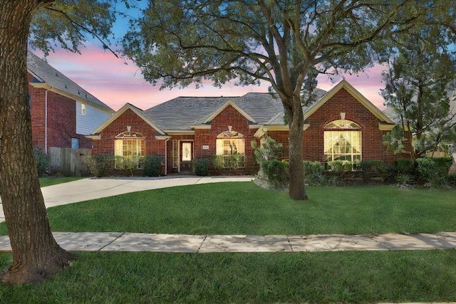 view of front of house featuring fence, a lawn, and brick siding