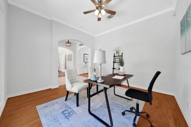 office area with baseboards, arched walkways, ceiling fan, ornamental molding, and wood finished floors