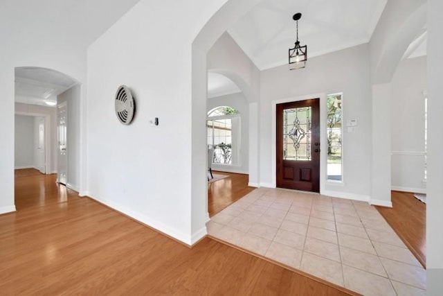 entryway featuring light wood-type flooring, baseboards, arched walkways, and ornamental molding