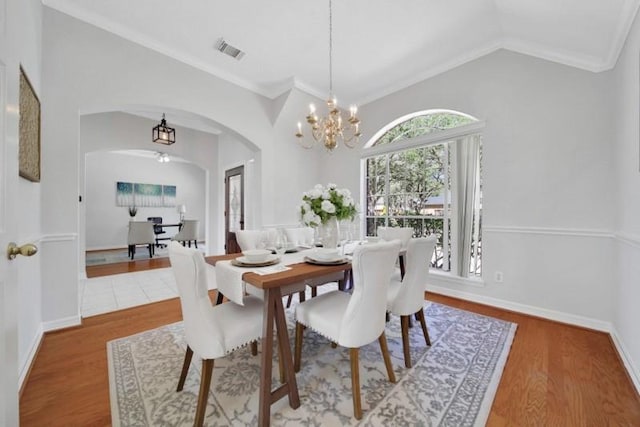 dining area with arched walkways, lofted ceiling, wood finished floors, visible vents, and ornamental molding